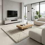 A modern living room featuring a light wood rectangular coffee table with black metal legs, styled on a large cream shag rug. The room has a white media console with a wall-mounted flat-screen TV, a cream boucle sofa, and a black multi-arm floor lamp.